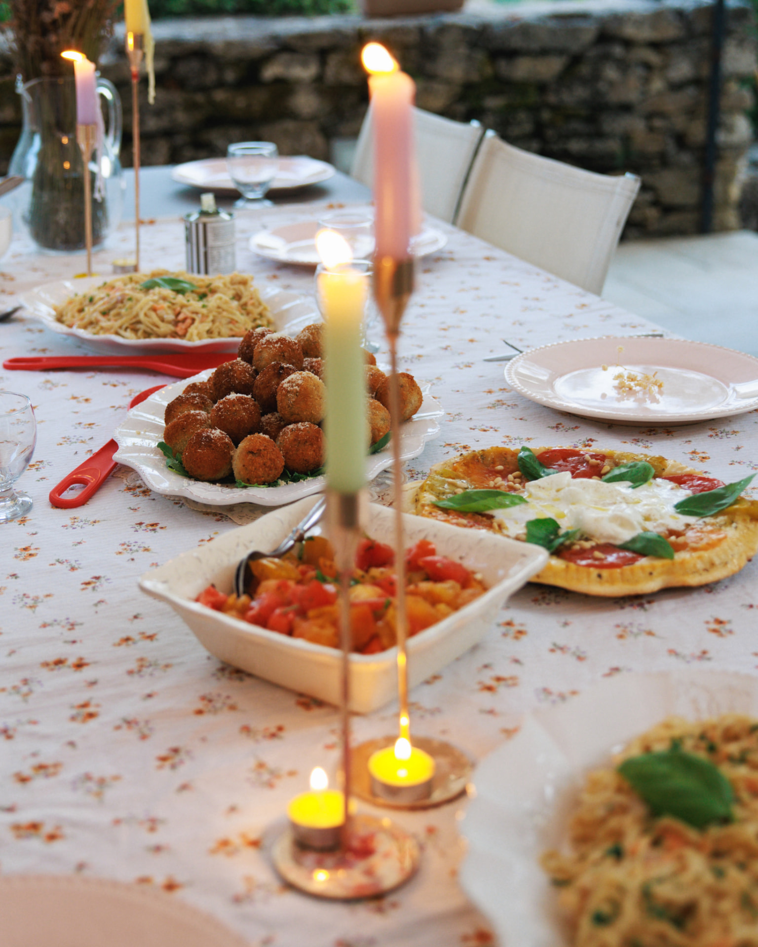 Table dressée avec nappe fleurie, bougies roses et arancinis
